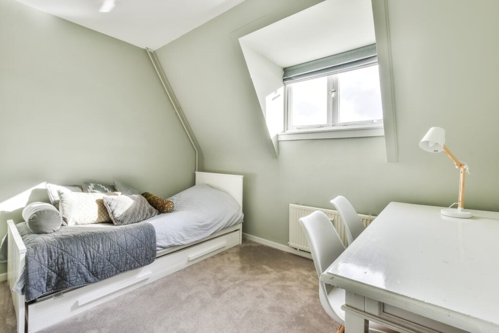 A small room with a single bed and table in the concept of 'how to pack household items safely for a move to Ealing'.